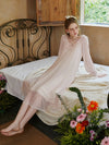 Woman sitting on bed wearing soft pink princess sleep dress in vintage bedroom