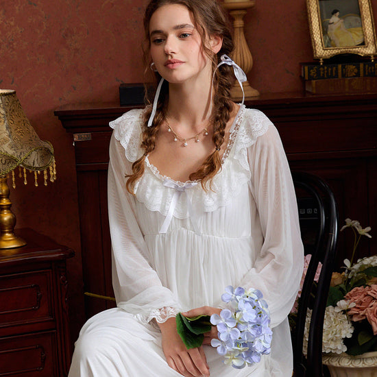 Seated view of the white lace nightgown showing translucent sleeves and softly gathered skirt layers
