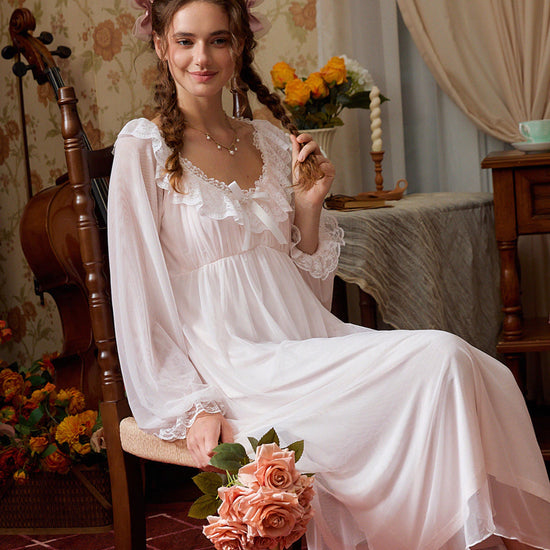 Seated view of the pink lace nightgown showing its sheer sleeves, soft lining, and romantic drape