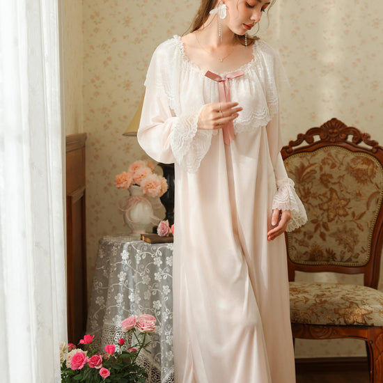 Standing three-quarter view of the light pink nightgown with a ribbon bow, flared lace cuffs, and a flowing long skirt