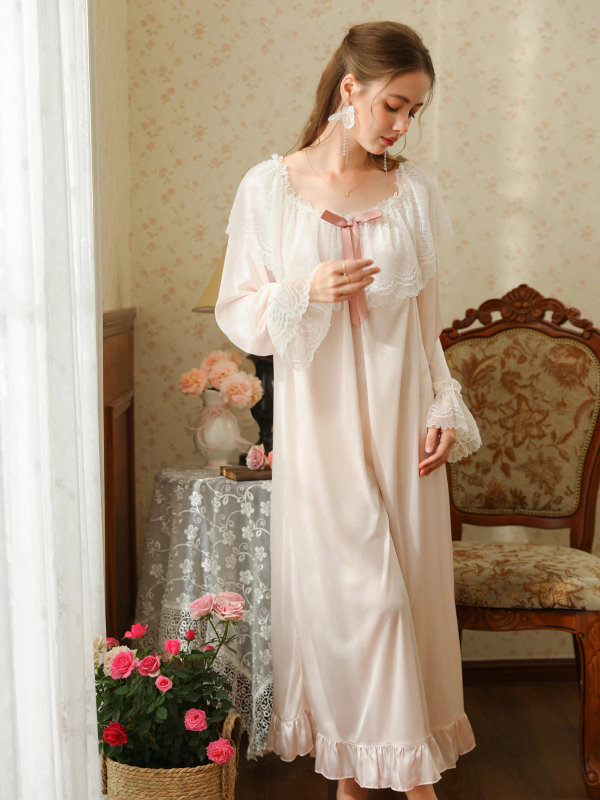 Standing three-quarter view of the light pink nightgown with a ribbon bow, flared lace cuffs, and a flowing long skirt