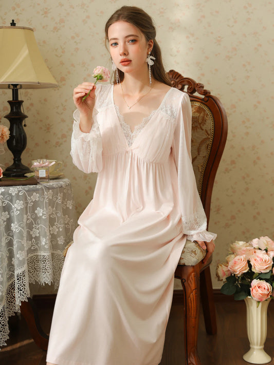 Seated front view of the pink nightgown with a lace V neckline, small ribbon bow, and sheer long sleeves