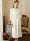 Front view of the white cotton nightgown showing its sheer embroidered yoke, scalloped lace bib, satin bow, and midi hem
