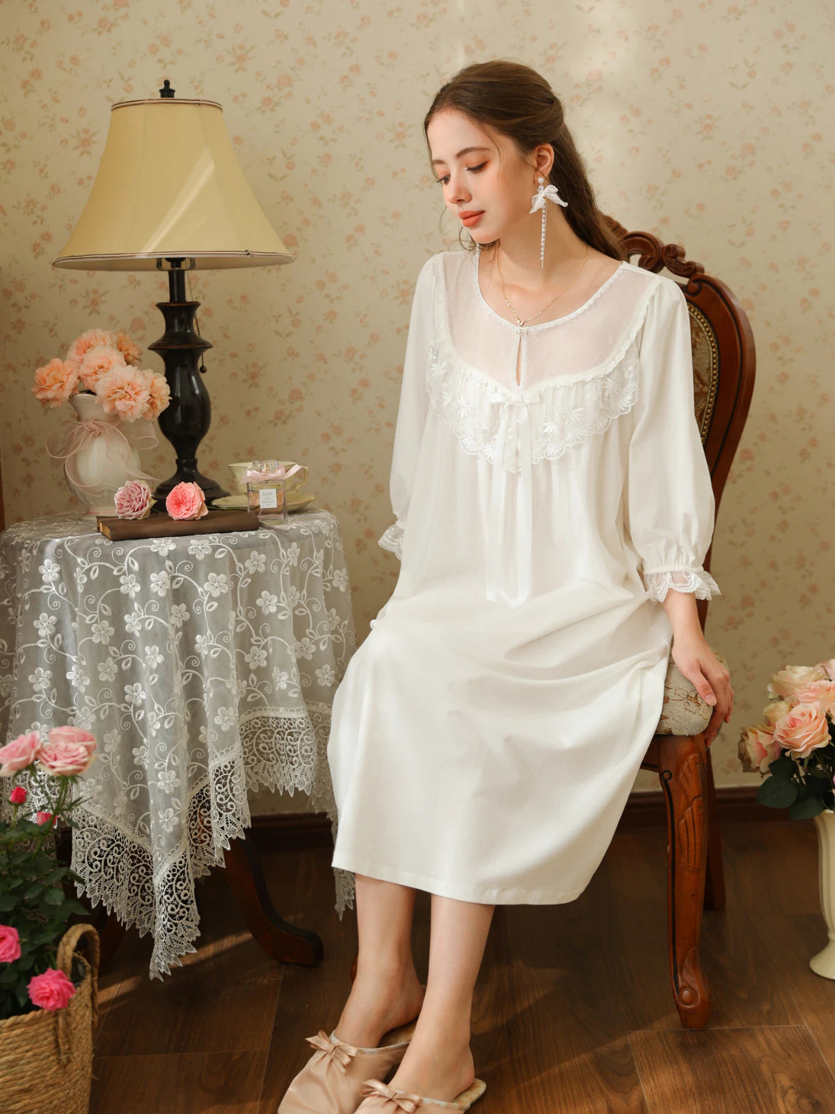 Seated view of the white cotton lace yoke nightgown showing its loose skirt drape and long satin ribbon bow
