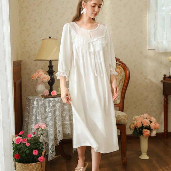 Full-length angled view of the white cotton nightgown showing the gathered sleeves, scalloped cuffs, and flowing midi silhouette