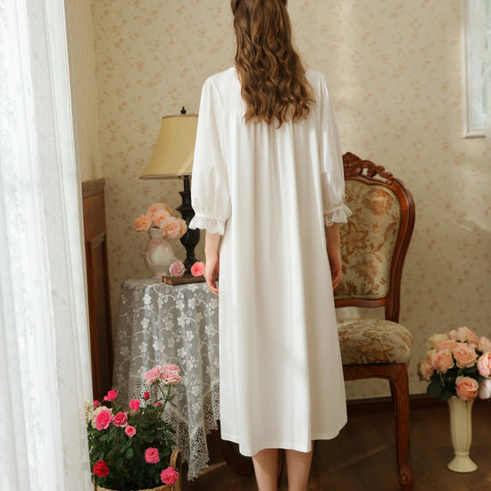 Back view of the white cotton nightgown showing the gathered back yoke, relaxed skirt, and lace trimmed sleeve cuffs