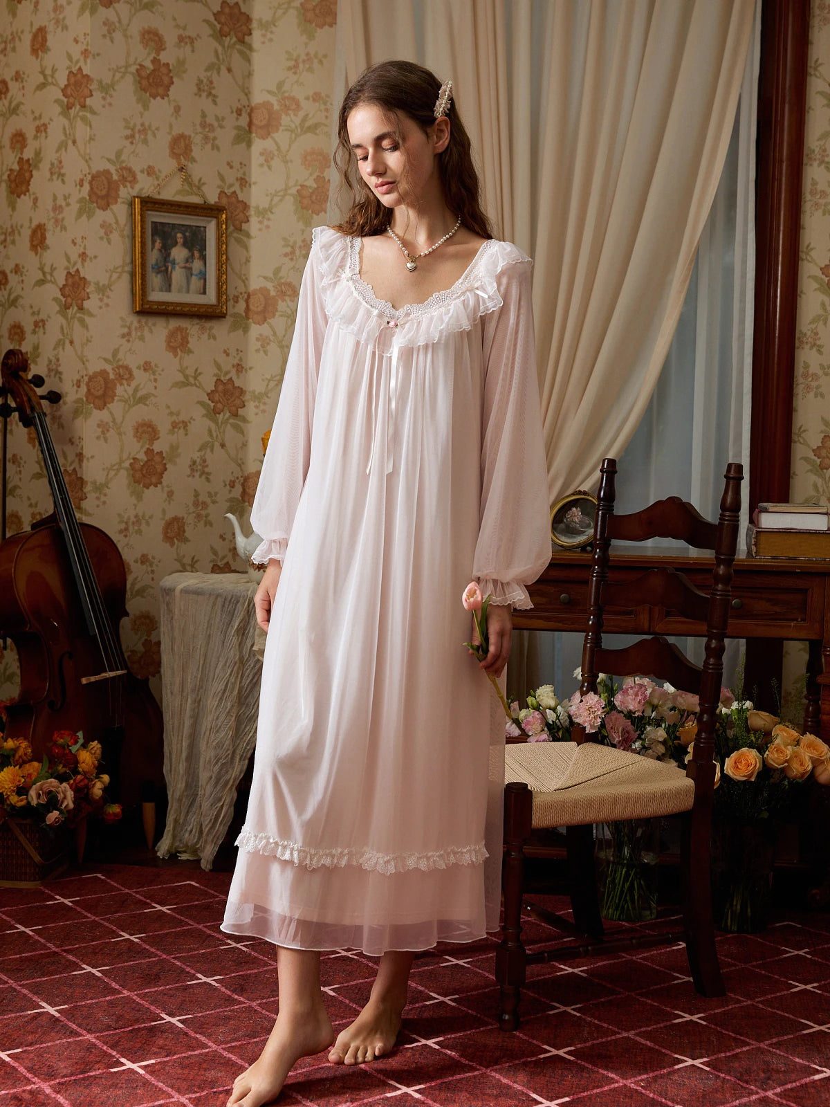 Full-length light pink nightgown with long sheer sleeves and a floral lace band above the translucent hem