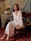 Seated view of the light pink lace nightgown highlighting its lined skirt, sheer sleeves, and scalloped lower lace band