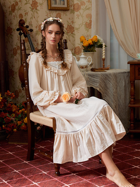 Seated view of the light yellow cotton nightgown with a white eyelet neckline, gathered long sleeves, and wide ruffle hem