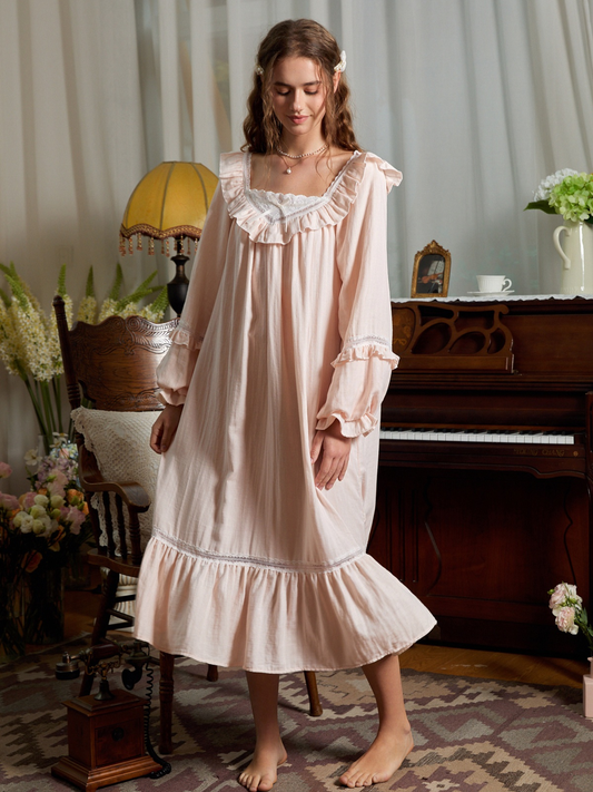 Full front view of the light pink cotton nightgown with a white lace neckline, gathered long sleeves, and ruffled hem