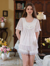 Seated view of the light pink short pajama set highlighting the lace bib and layered ruffles