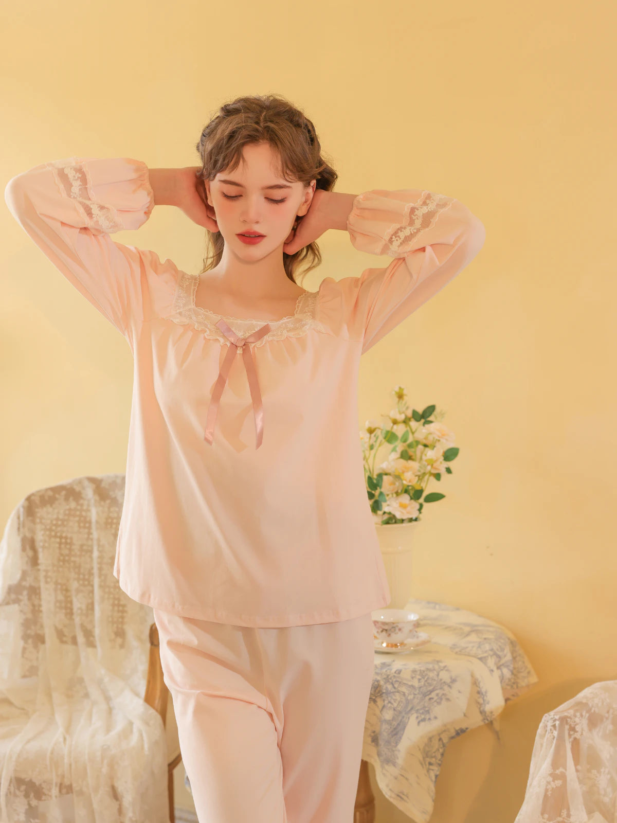 Seated view of the pink pajama set highlighting its soft drape and floral lace insets